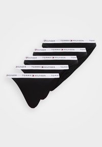 Πέντε μαύρα εσώρουχα Tommy Hilfiger στοιβαγμένα, καθένα με άσπρη μέση που φέρει το όνομα της μάρκας και το λογότυπο σε μαύρο και κόκκινο.