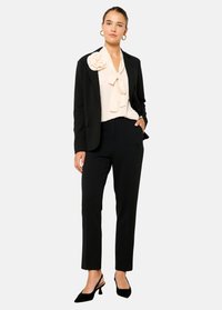 Črn krojen blazer čez svetlo bluzo z velikim blago cvetom. Črne slim-fit hlače in črne pointe pete dopolnjujejo videz.