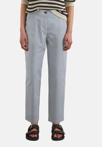 Pantalons en coton gris clair avec une coupe droite, dotés d'une fermeture à un bouton, portés avec des sandales noires mettant en valeur un accent doré.
