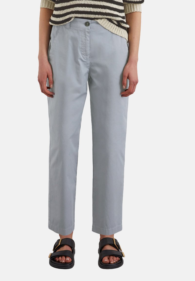 Pantalons en coton gris clair avec une coupe droite, dotés d'une fermeture à un bouton, portés avec des sandales noires mettant en valeur un accent doré.