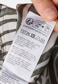 Label on a garment: white with care instructions. Text includes fabric content (85% viscose, 15% nylon), wash instructions, and multilingual details.