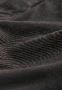 Mörk tyg med en mjuk, texturerad yta och subtil ribbstruktur som visar en lätt lyster i varierande ljus.