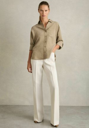 Chemise en lin beige à boutons avec manches retroussées, assortie à un pantalon large blanc, présentant une coupe droite et un léger éclat.