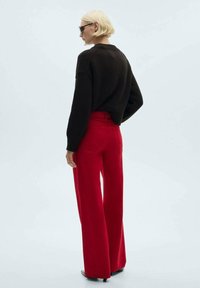 Bruine gebreide trui gecombineerd met wijde rode broek. De outfit heeft een relaxte pasvorm en een soepele afwerking, met subtiele achterzakken.