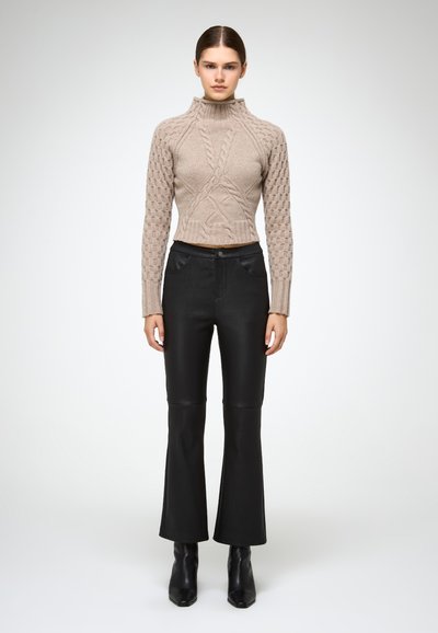 Jersey de cuello alto beige de punto con patrones de trenza, combinado con pantalones de pierna acampanada negros de talle alto y botas de tobillo negras.