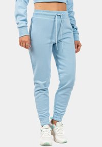 Lichtblauwe trainingsbroek gemaakt van zachte stof, met een elastische tailleband met trekkoord, zijzakken en aangesloten boorden bij de enkels.