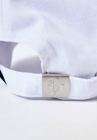 Gorra de algodón blanca con tejido texturizado; presenta un cierre de metal plateado con logotipo en relieve; diseño minimalista con una correa ajustable.