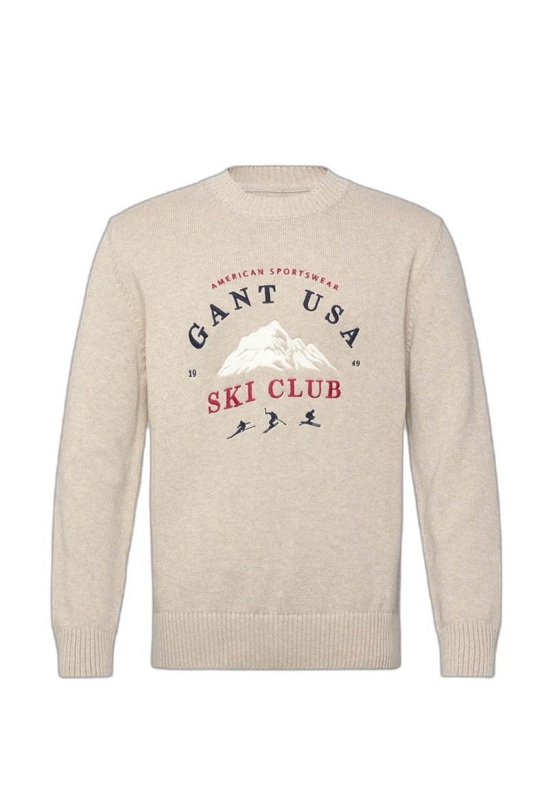 Maglione beige a maglia con grafica di montagna e testo "Gant USA Ski Club," con tre silhouette di sciatori sotto il disegno.