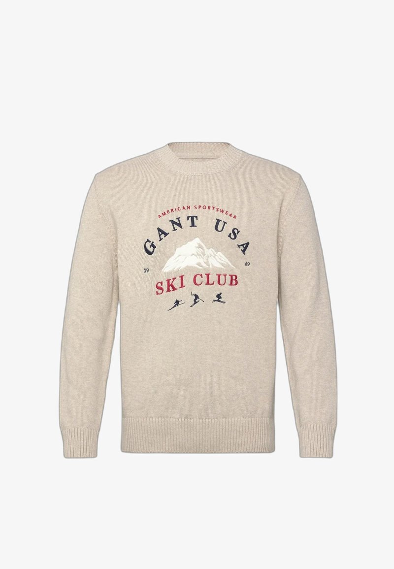 Maglione beige a maglia con grafica di montagna e testo "Gant USA Ski Club," con tre silhouette di sciatori sotto il disegno.