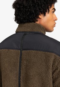 Brown fleece jacket with a textured finish, black nylon shoulders, and contrasting stitching along the back and collar.