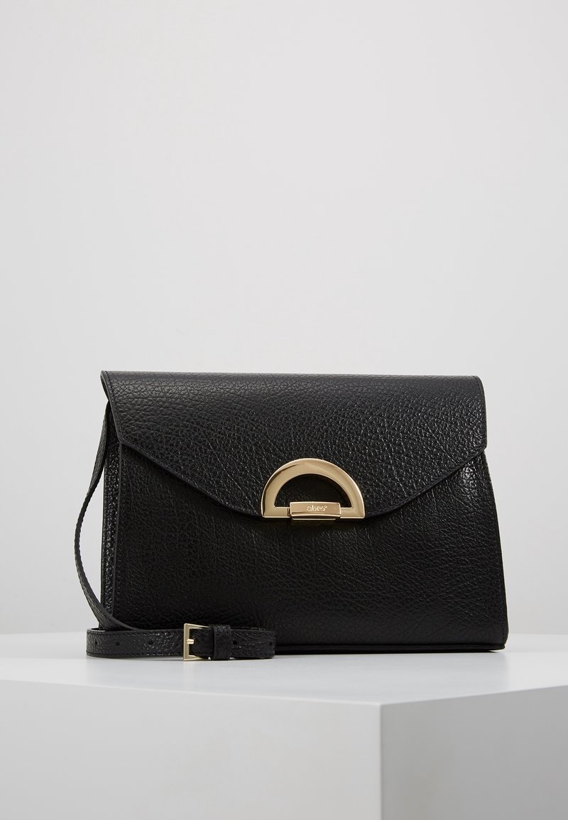 Borsa a tracolla in pelle nera texturizzata con chiusura a patta angolata, fibbia circolare dorata e tracolla removibile.