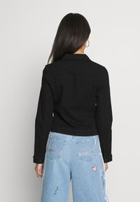 Svart denimjacka med krage, långa ärmar och cropped design. Har förstärkt sömnad och en slät textur.