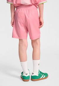 Rosa shorts med elastisk midja, kombinerat med gröna sneakers, vita strumpor och en rosa randig skjorta med gröna detaljer.