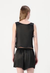 Satin svart sengetøy-sett med en ermeløs topp med rund hals og løstsittende shorts med elastisk midje.