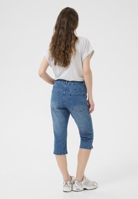 Blå denim capri-jeans med hög midja, medellång klippning och två bakfickor. Tyget har en slät textur och en lätt stretch.