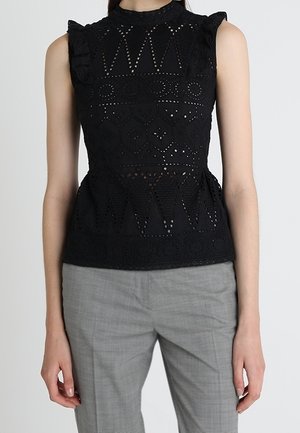 Top negro sin mangas de encaje con recortes geométricos y detalles de volantes combinado con pantalones a medida en gris claro.