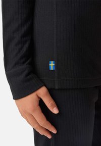 Czarny prążkowany termiczny top z długimi rękawami, z małym akcentem w postaci niebiesko-żółtej flagi szwedzkiej na dolnym końcu. Miękki, elastyczny materiał.