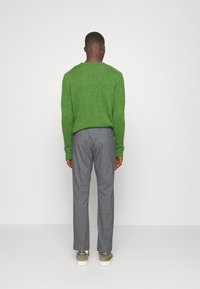 Pull vert en tricot, pantalon gris cintré et baskets grises. Texture tricotée sur le pull, tissu lisse sur le pantalon, lacets plats.