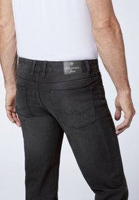 Black jeans made of denim, featuring a straight-leg design, back pockets, and a label reading "OKLAHOMA" on the waistband.