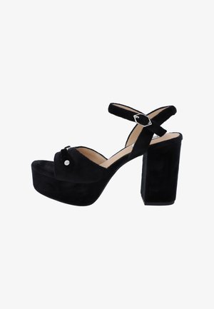 Sandali platform in suede nera con tacco chunky, cinturini incrociati alla caviglia e un accento metallico decorativo sulla fascia frontale.