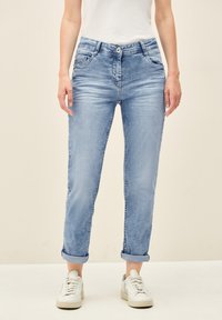 Jeans en denim bleu clair avec des ourlets retroussés, une fermeture à bouton et des poches avant. Le tissu a une texture délavée avec de subtils détails de froissement.