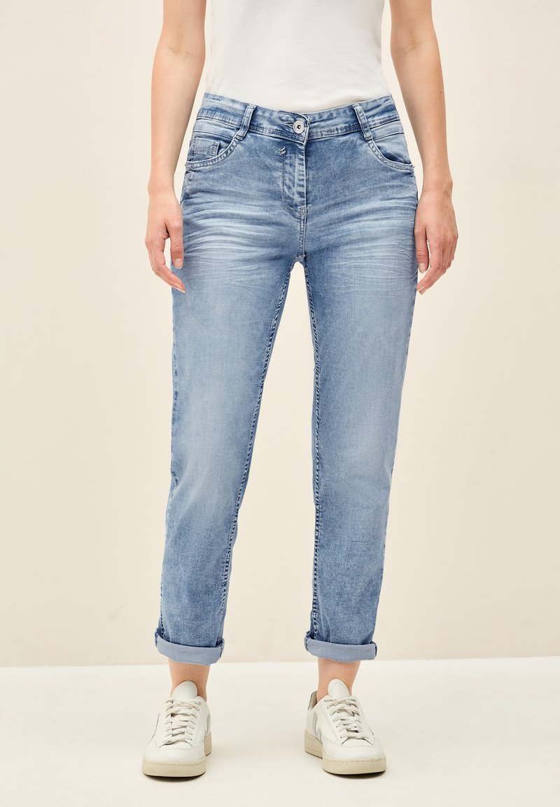 Jeans en denim bleu clair avec des ourlets retroussés, une fermeture à bouton et des poches avant. Le tissu a une texture délavée avec de subtils détails de froissement.