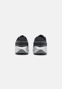 Vista posteriore di scarpe sportive nere con una suola intermedia in argento imbottita e una suola esterna in gomma testurizzata, caratterizzate da un design minimalista e senza loghi visibili.