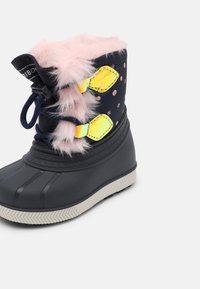Botte d’hiver enfant avec semelle en caoutchouc noire, dessus en tissu bleu marine à pois roses, bordure en fausse fourrure rose et bandes réfléchissantes jaunes.