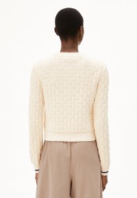Cremfarbener gestrickter Pullover mit einem strukturierten Muster, gerippten Bündchen und einem kurz geschnittenen Design. Sichtbarer Pullover-Saum und weiches Material.