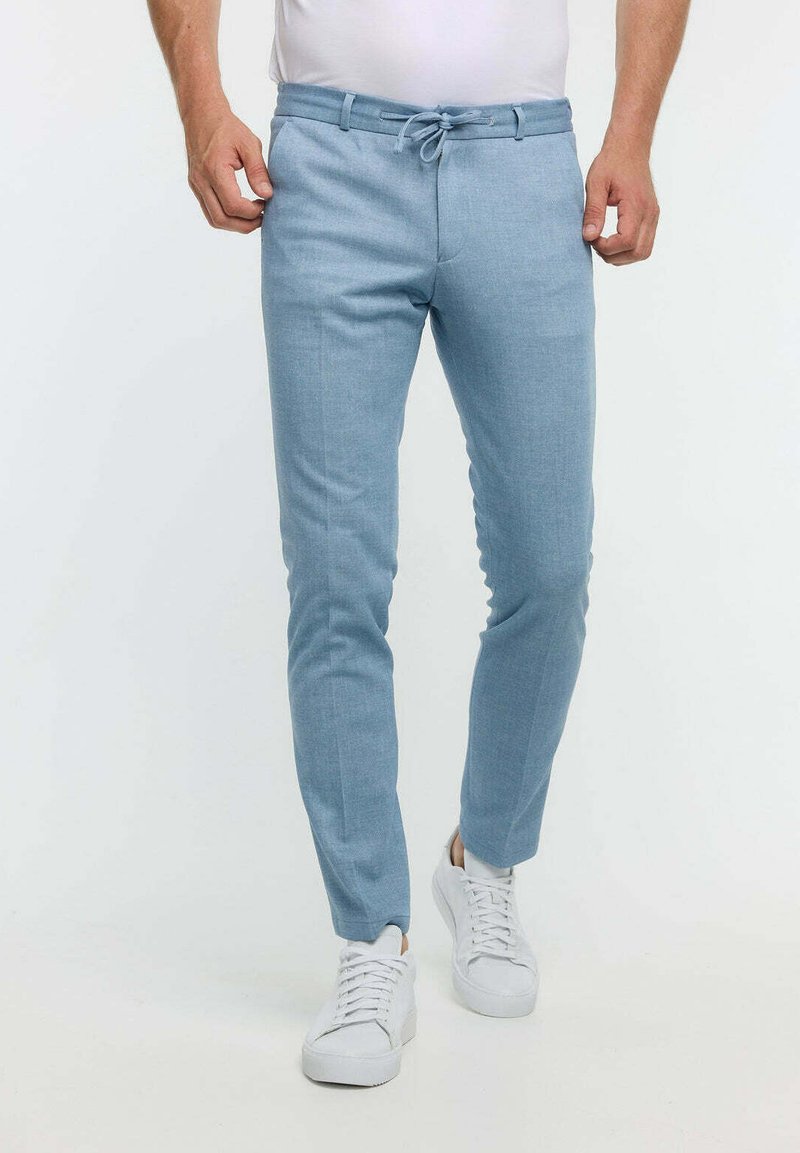 Helleblaue, maßgeschneiderte Hose aus weichem Stoff mit Kordelzugbund, schmaler Passform und Fronttaschen. Kombiniert mit weißen Sneakern.