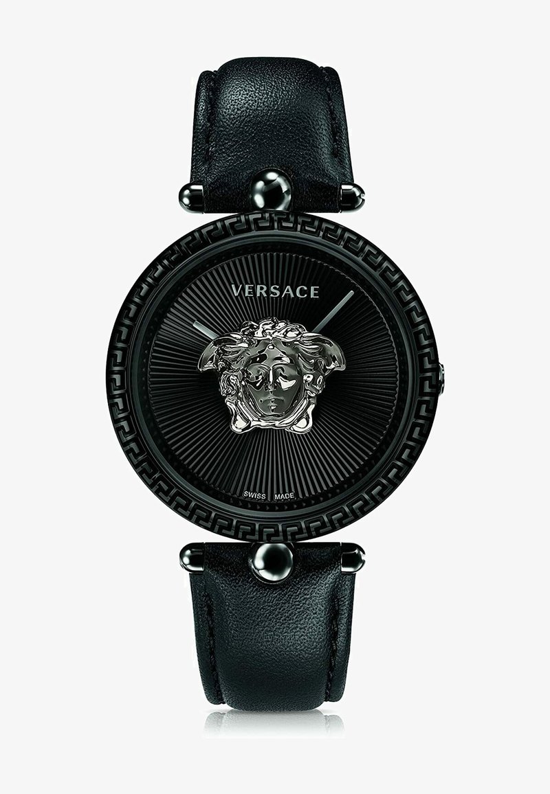 Black leather strap watch with a round black dial, silver Medusa emblem, textured background, and Greek key design on the bezel.