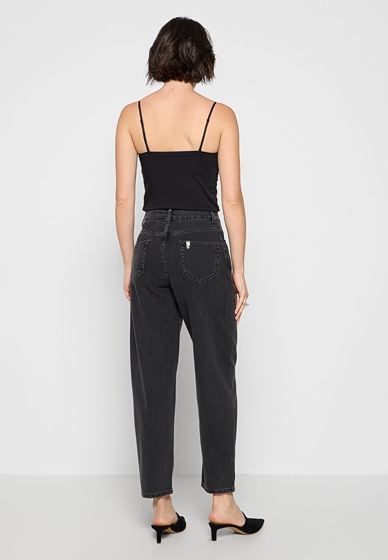 Top negro sin mangas con tirantes finos, combinado con jeans oscuros de cintura alta y corte suelto. Diseño minimalista, textura suave, ajuste de altura media.