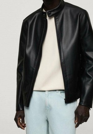 Czarna kurtka z imitacji skóry z wysokim kołnierzem, przednim zamkiem błyskawicznym i długimi rękawami, zestawiona z jasnym swetrem i dżinsami.