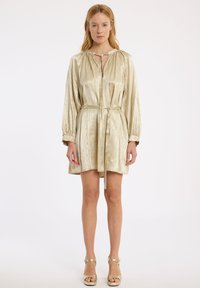 Robe dorée métallisée à manches courtes, en tissu soyeux, avec un col à nouer, des épaules froncées et une taille ceinturée.
