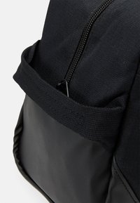 Black backpack featuring a textured fabric and a smooth, matte lower section. Includes an exterior zippered pocket for storage.