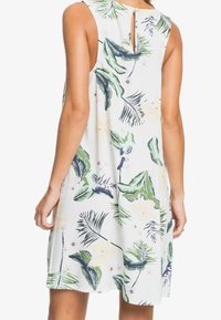 Robe blanche sans manches avec un motif de feuilles tropicales en vert et marine. Présente un détail dos en trou de serrure et une coupe décontractée.