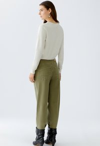 Beige langärmliges Oberteil mit Rundhalsausschnitt, kombiniert mit olivgrünen locker geschnittenen Hosen mit Gesäßtaschen und schwarzen lässigen Ankle-Boots.