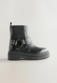 Sorte læder ankelstøvler med en kraftig sål, dekorativ rem med en cirkulær metalaccent og elastiske sidelapper for nem påtagning.