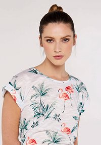 T-shirt blanc avec un motif de feuilles de palmier vertes et de flamants roses, manches courtes, texture douce, col rond, coupe décontractée.