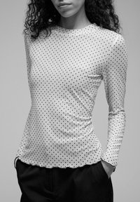 Długi rękaw, wykonany z lekkiego materiału, z białą bazą i czarnymi kropkami oraz dopasowanym krojem z zaokrąglonym dołem.