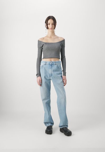 Gray off-the-shoulder ribbed crop top paired with light blue loose-fit jeans, worn with black clogs. Background is minimalistic and white.