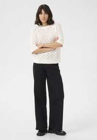 Witte gebreide trui met diamantenpatroon, korte mouwen, gecombineerd met zwarte high-waisted wijde broek en glanzende zwarte schoenen.