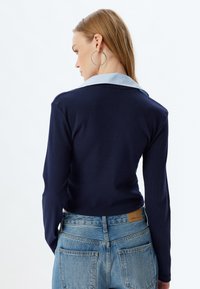Marineblaues Langarmoberteil mit geripptem Muster und hellblauem gestreiften Kragen. Kombiniert mit hellblauen Jeans aus Denim mit Gesäßtaschen.