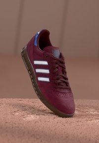 Burgundy mockasiner i mocka med blå accenter, har tre vita ränder och en texturerad brun gummisula, designad för vardagsbruk.