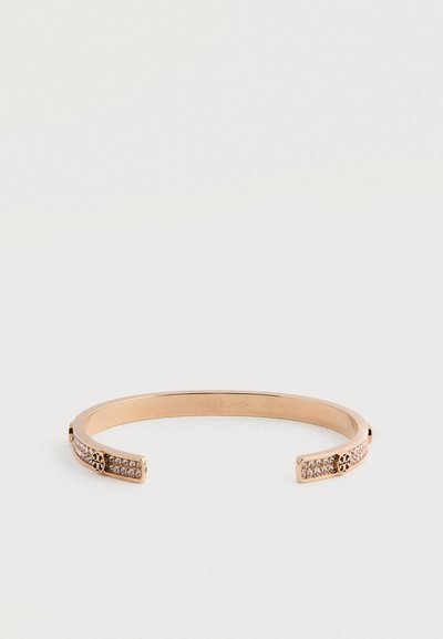 Bracelete aberto em ouro rosa com cristais embutidos e acabamento com o logotipo da Tory Burch em cada extremidade, em contraste com um fundo simples.