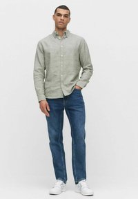 Lichtgrijze button-up shirt in een gestructureerde stof, gecombineerd met donkerblauwe jeans en witte sneakers. Het shirt heeft een klassieke kraag en lange mouwen.