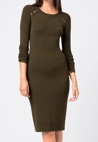 Olivgrön ribbad klänning med långa ärmar, åtsittande form och metalliska detaljer vid axelsömmarna. Slät textur med knälång fåll.