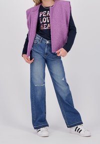 Purple fuzzy vest over a black long-sleeve shirt with "PEACE LOVE HEART" text, paired with light blue wide-leg jeans and white sneakers.