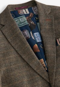 Bruine blazer met patroon en een gestructureerde stof. Vanbinnen voorzien van een blauwe voering met diverse vintage kaartontwerpen en accenten.
