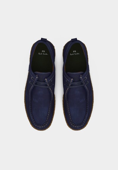 Ζευγάρι λευκών casual παπουτσιών από δέρμα σε ναυτικό μπλε με κορδόνια, ραμμένες λεπτομέρειες και καφέ σόλες από καουτσούκ, σε προβολή από πάνω.